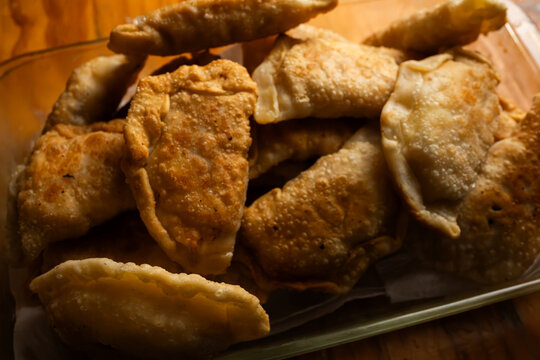 Close up shot of freshly fried golden brown empanadas stacked in a glass dish