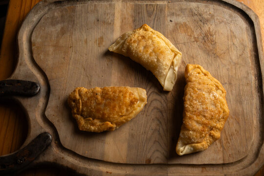 Top view of three freshly fried golden brown empanadas on a rustic wooden board