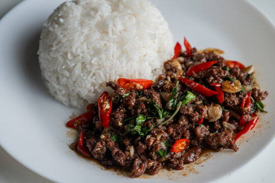 Thai stir-fried minced beef with holy basil and red chili served with steamed jasmine rice on a white plate.