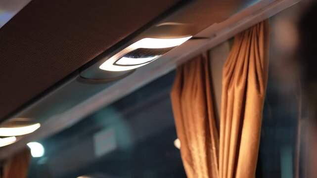 Person's hand turning on reading light in a modern bus cabin, traveling at night