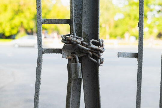A metal gate is locked with a rusty chain and padlock, preventing access to the area beyond. The setting is bright and sunny, suggesting a busy location nearby