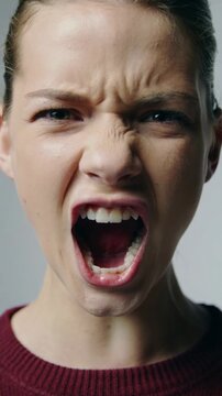 Young woman in burgundy sweater screaming with intense facial expression extreme close up