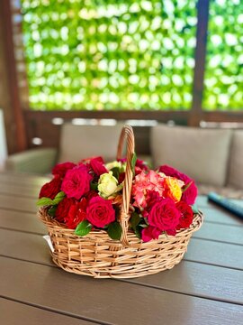 Cesta de mimbre con un hermoso arreglo de rosas rojas y rosadas sobre mesa exterior