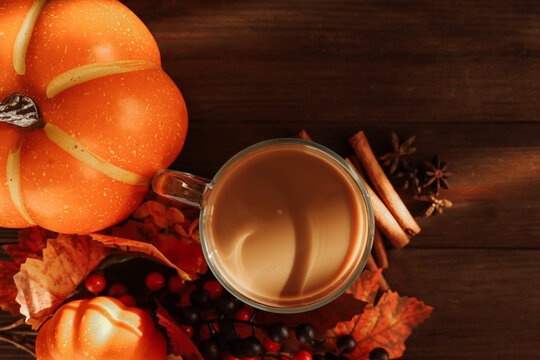 Enjoying pumpkin spice latte with pumpkins and autumn leaves on a wooden table in the fall season