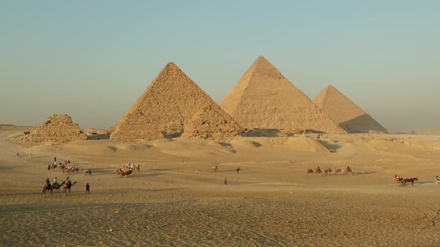Great Pyramid of Giza with camel riding tours on sandy plateau on clear day, tourist attractions. 
