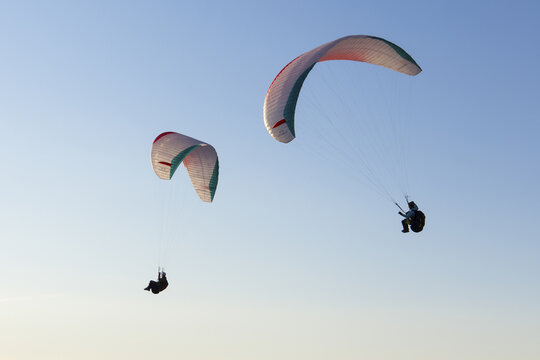 Aerial view of two paragliders soaring through the clear blue sky above the Dachstein mountain range in Grobming, Styria, Austria.