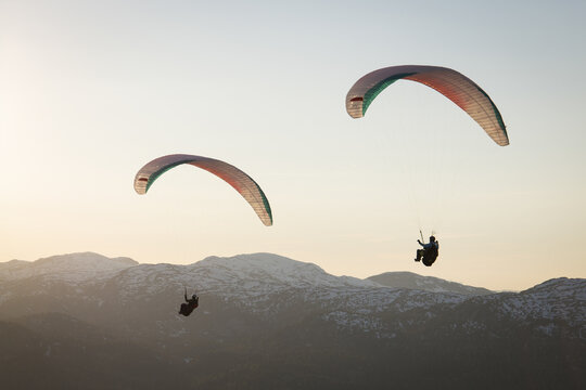Aerial view of paragliders soaring over the snow-capped peaks of the Dachstein mountains in the evening light in Grobming, Styria, Austria.