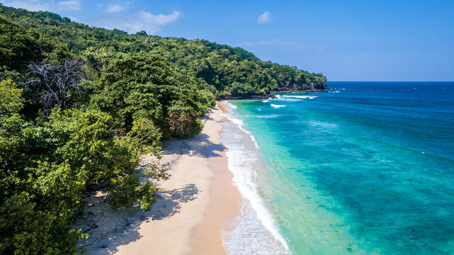 Aerial view of Waebela beach with turquoise waters, white sand, and dense tropical forest along the coastline in Inerie, East Nusa Tenggara, Indonesia.