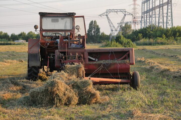 Tractor and hay baler working in a mown field at golden hour © Ionel