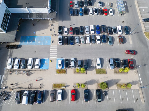 Aerial view of a shopping mall parking lot with rows of parked cars, marked accessible parking spaces, and small landscaped areas in Kempele, North Ostrobothnia, Finland.