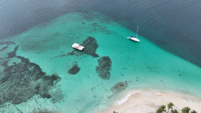 Aerial view of Cayo Levantado with turquoise waters, coral reefs, a catamaran, and a sailboat anchored off the sandy beach in Samana, Dominican Republic.