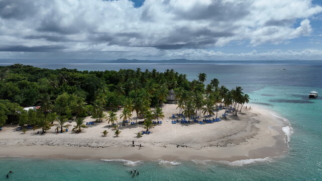 Aerial view of Cayo Levantado with lush palm trees, white sand beach, turquoise water, and people swimming in Samana, Dominican Republic.