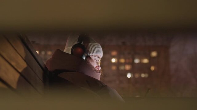 Hidden young woman behind railing city, intimate viewpoint through gap, phone screen glow, contemplative gaze, headphones muffling city noise, distant apartment lights, private cinematic moment