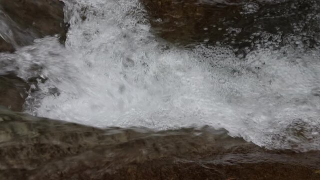 A stream in a whirlpool of water in a mountain stream, moving along a riverbed with air bubbles, close-up
