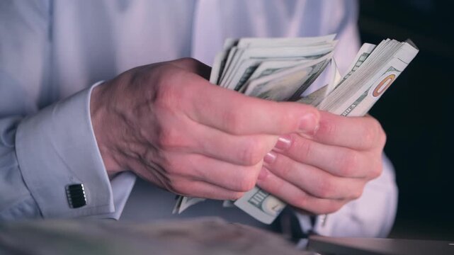 Businessman in a formal shirt counts a thick stack of American hundred dollar bills with his hands.