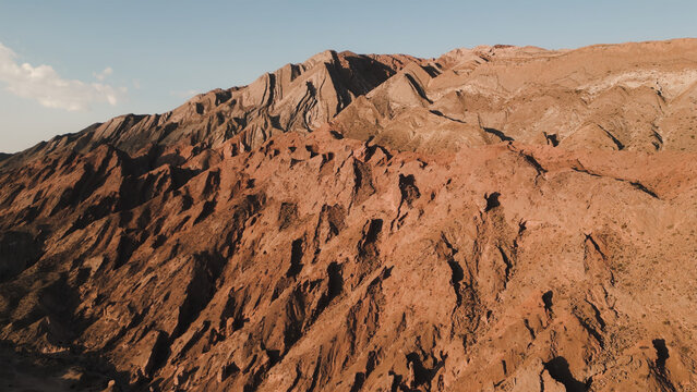 Aerial view of the rugged, arid, reddish-brown mountain landscape of the Valles Calchaquies, showcasing dramatic geological formations and steep slopes San Carlos, Salta, Argentina.