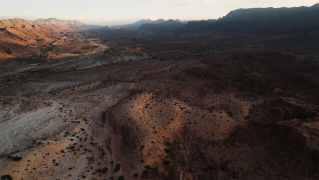 Aerial view of Valles Calchaquies featuring arid desert terrain, rugged mountains, and deep shadows cast during golden hour in San Carlos, Salta, Argentina.