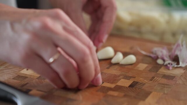 Woman peels garlic cloves by hand on a wooden cutting board. Concept of home cooking and everyday meal making