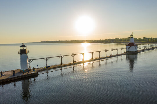 Aerial view of St. Joseph North Pier lighthouses and pier extending into Lake Michigan at sunset with fishermen standing on the concrete walkway in St. Joseph, Michigan, United States.