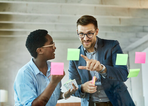Portrait of young businesswomen and businessman meeting at office and using sticky notes on glass to share idea. Brainstorming and teamwork concept. Sticky note on glass wall.
