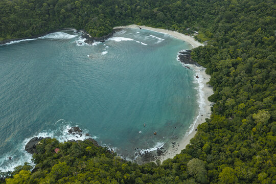 Aerial view of Pantai Wedi Ireng with its secluded sandy beach, turquoise waters, and dense tropical forest surrounding the coastline in Pesanggaran, East Java, Indonesia.