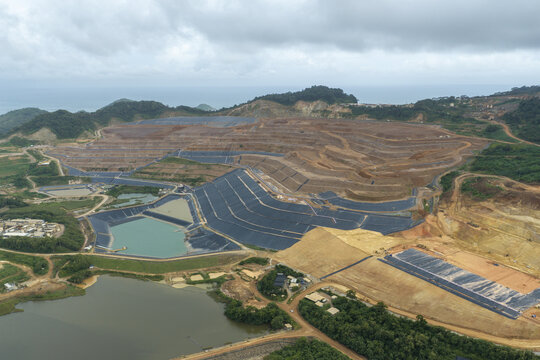 Aerial view of the large open-pit gold and copper mine featuring terraced excavation sites, industrial tailings ponds, and surrounding tropical landscape in Java, Indonesia.