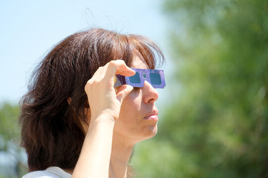 Woman looking to sun eclipse with special glasses. Solar eclipse glasses are specially certified, ultra-dark glasses to protect eyes from damage when looking directly at sun.