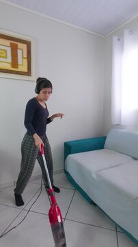 Happy woman wearing headphones dancing and singing while cleaning the living room with a vacuum cleaner