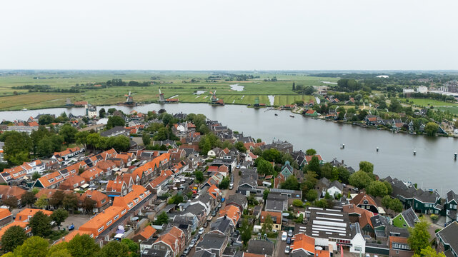 Aerial view of the historic Zaanse Schans with its iconic windmills, traditional wooden houses, and lush green fields along the Zaan river in Zaandam, North Holland, Netherlands.