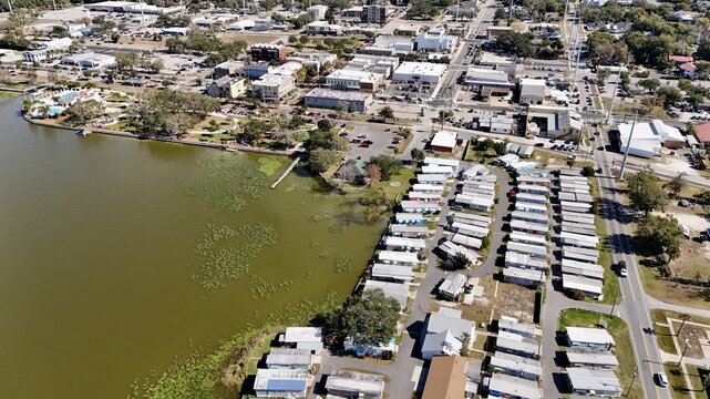 Aerial view of a mobile home park along the shore of a lake in the town of Eustis, with surrounding residential streets, commercial buildings, and trees in Eustis, Florida, United States.