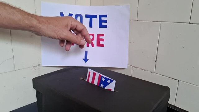 Hand inserting american flag ballot paper into black box