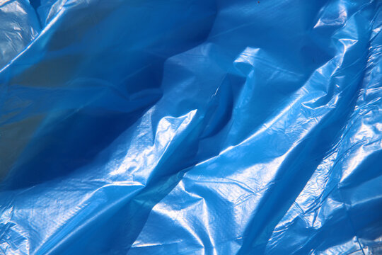 Crumpled blue texture of cling film, polyethylene film close up photo, art project, design background. Dangerous material for the environment concept