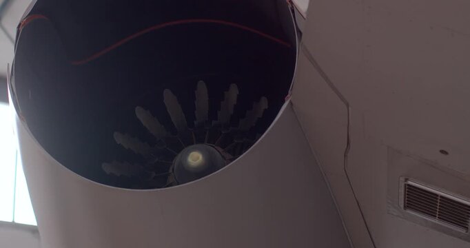 Dramatic shot highlighting circular turbine pattern under dim lighting. Close examination of jet engine fan revealing intricate spinner and blade root arrangement in museum setting