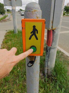 Hand pressing pedestrian button at street intersection