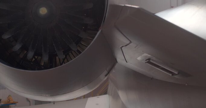 Flap track housing and engine pylon closeup showing panel seams, vents and nacelle inlet during underwing inspection and servicing in hangar. Focus on hydraulic track, attachment