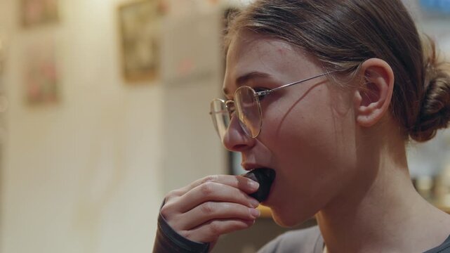 Happiness evident as woman delightfully samples delicious chocolate in warm environment. Joyful young woman indulges in rich chocolate treat under inviting ambient lighting conditions