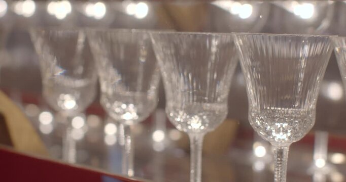 Fluted stemware in sparkling display, closeup of crystal goblets on rowed shelf with bokeh highlights and shimmering reflections, delicate stems and etched bowls, elegant event