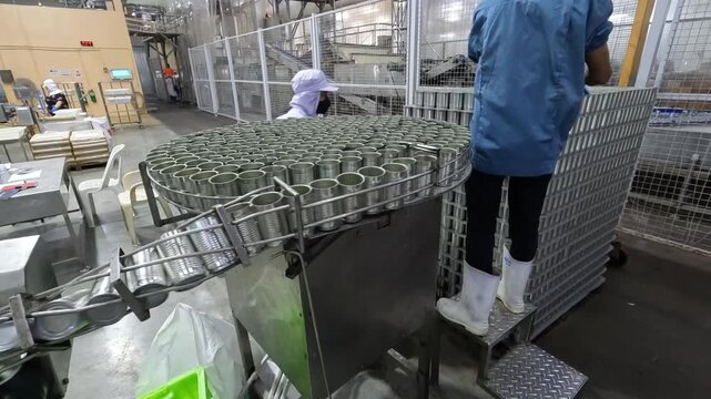 Workers operate machinery in a factory producing canned goods in an industrial setting
