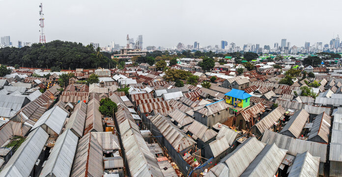 Aerial view of Karail slum with dense corrugated metal rooftops and a vibrant blue and yellow house, set against the urban skyline of Dhaka, Dhaka Division, Bangladesh.