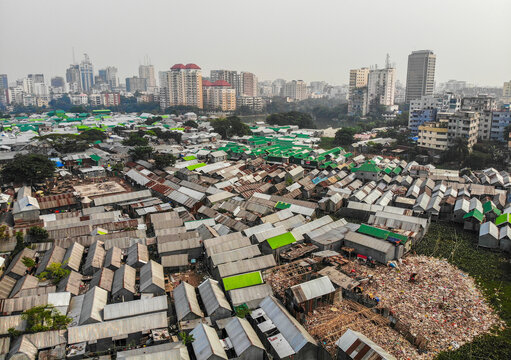 Aerial view of Karail slum featuring dense rows of metal-roofed houses with green accents and the urban skyline of Dhaka in the background, Dhaka, Dhaka Division, Bangladesh.