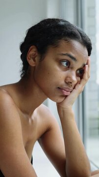 Young multiracial woman resting head on hand looking out window indoors close up shot