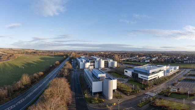 Aerial view of New College Durham, University white office buildings, parking lots, and surrounding green fields in Durham, England, United Kingdom.