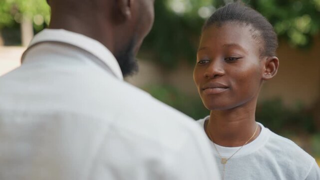 Black couple in honest date conversation in leafy courtyard, woman expresses feelings while man listens over shoulder, closeup expressions shift from playful to pensive, soft daylight, emotional