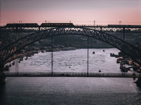 Aerial view of the iconic Luis I Bridge spanning the Douro River with a metro train crossing the upper deck and boats on the water in Porto, Porto District, Portugal.