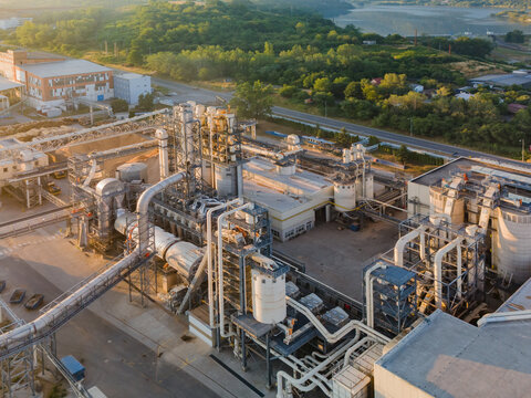 Aerial view of the Kronospan woodworks facility featuring industrial pipes, storage tanks, and machinery surrounded by trees during golden hour in Zvolen, Banskobystricky kraj, Slovakia.