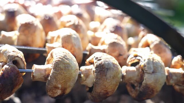 Golden-brown mushrooms sizzle on a grill. Smoke rises gently. Round caps curl slightly. Close-up shows grill marks. Ideal for cooking food videos. Fresh and appetizing