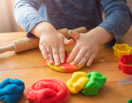 A close-up shot captures a child's hands skillfully molding colorful playdough on a rustic wooden table, with a rolling pin and various sculpting tools scattered around the creative workspace.
