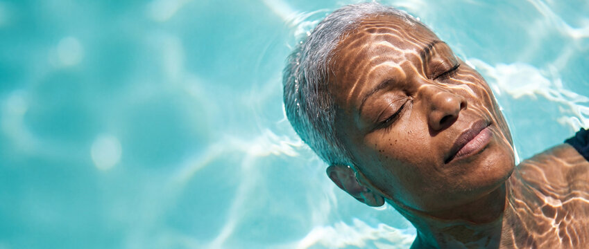 Senior woman floating in swimming pool with eyes closed under bright sunlight, captured in crystal clear turquoise water for wellness, retirement, stress relief, and vacation concepts