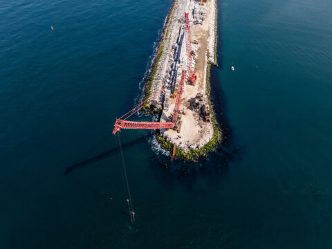 Aerial view of heavy-duty lattice-boom crawler cranes working on a breakwater with concrete blocks and deep blue sea in Matosinhos, Porto District, Portugal.
