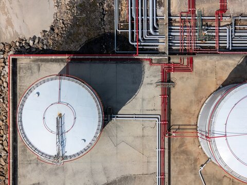 Aerial view of LNG silos with intricate red piping and industrial infrastructure on a concrete surface in Matosinhos, Porto, Portugal.